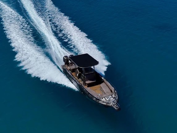A speedboat crossing deep blue water, seen from above, its wake curving out behind it